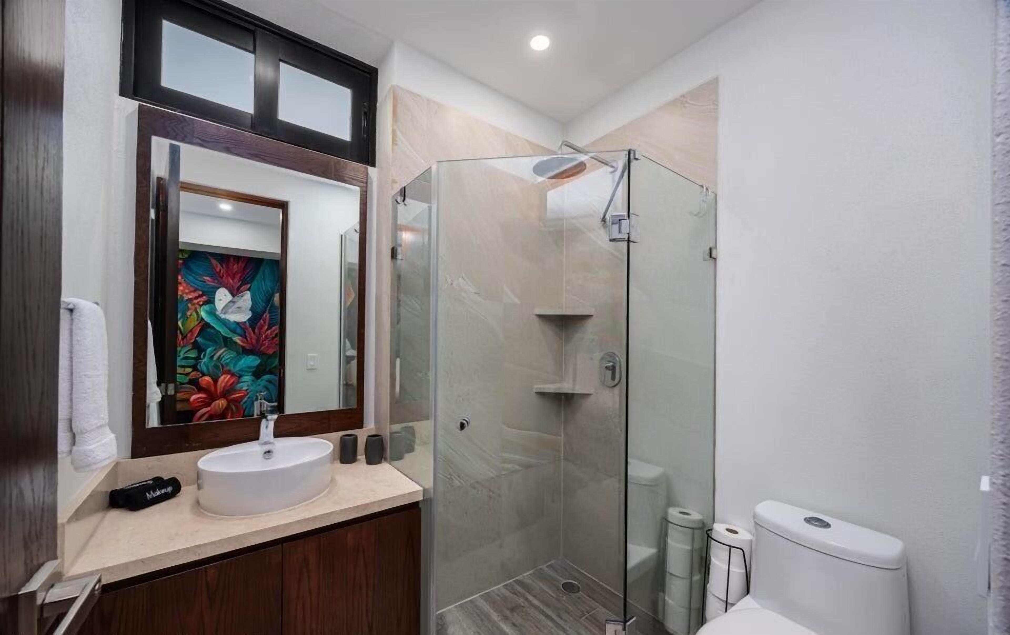 Un bagno moderno con cabina doccia in vetro, lavandino bianco e mobile bagno in legno.