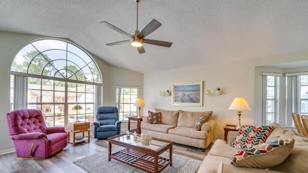 A spacious living room with a large arched window, a ceiling fan, and a beige sofa.