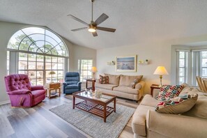 A spacious living room with a large arched window, a ceiling fan, and a beige sofa. - Spacious 3-bedroom condo with pool and fitness room near to Disney for 8 People (Kissimmee)