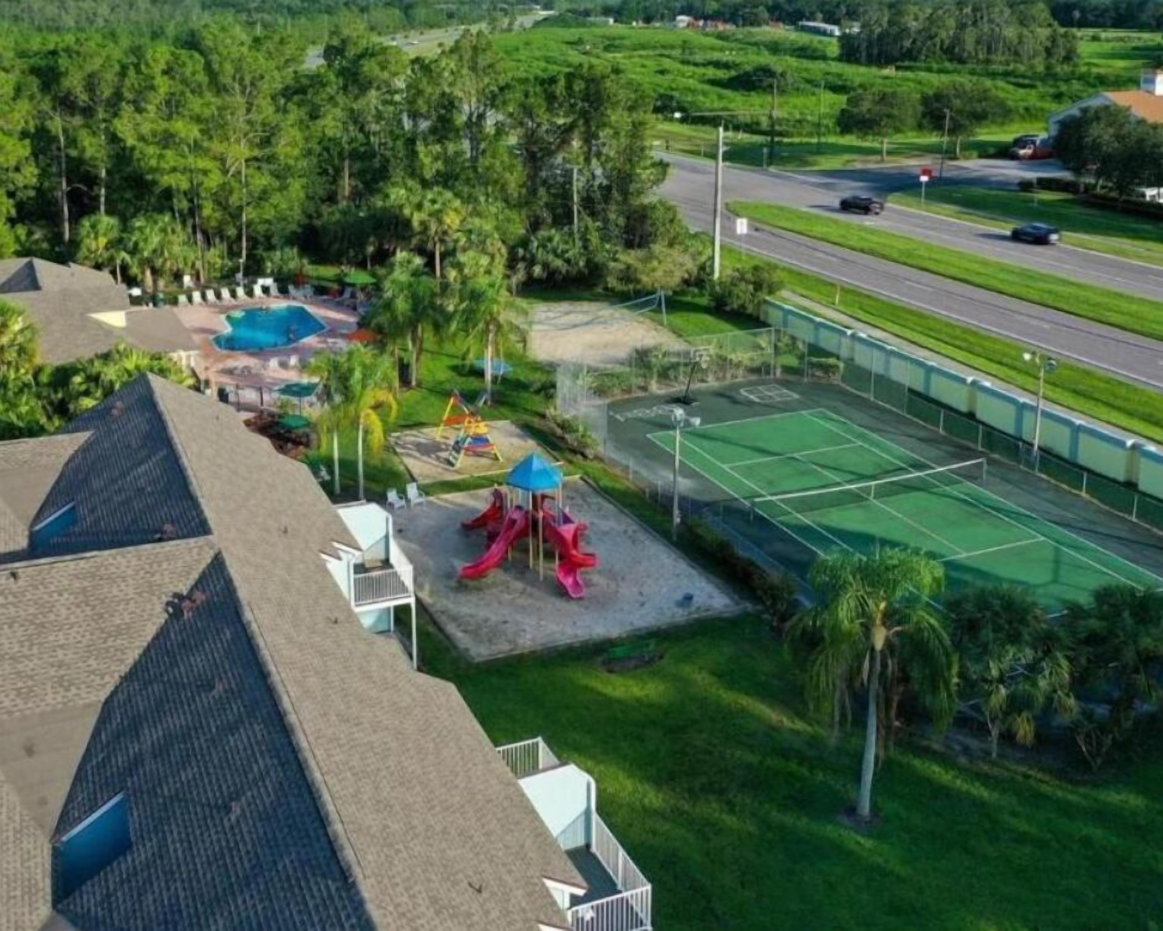 A residential area with a tennis court, playground, and a road with vehicles.