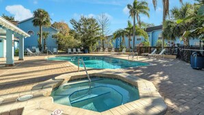 A pool area with lounge chairs, a hot tub, and palm trees.