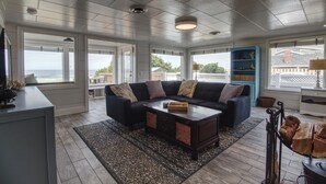 A spacious living room with a dark-colored sofa, a wooden coffee table, and a view of the ocean through large windows.