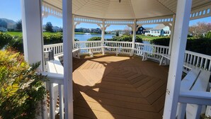 A gazebo with a wooden floor and white railings, overlooking a lake and houses.