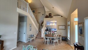 A spacious living area with a dining table, chairs, and a staircase leading to an upper level.
