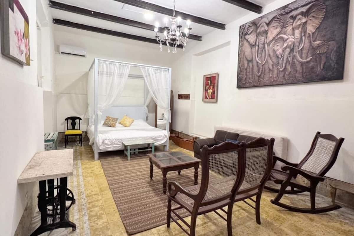 A bedroom with a bed, a sitting area with chairs, a table, and a large artwork on the wall.