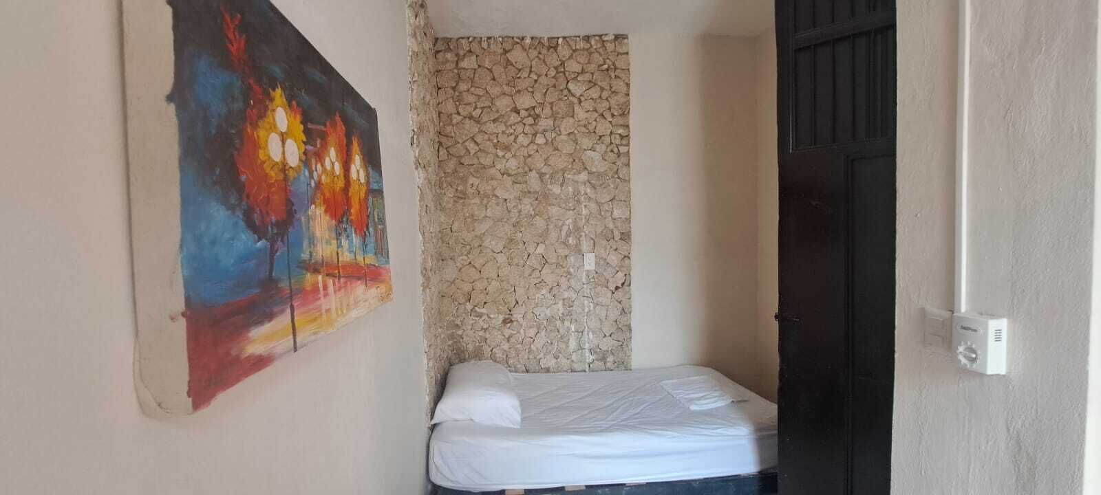 A room with a bed, a stone wall, and a colorful painting on the wall.