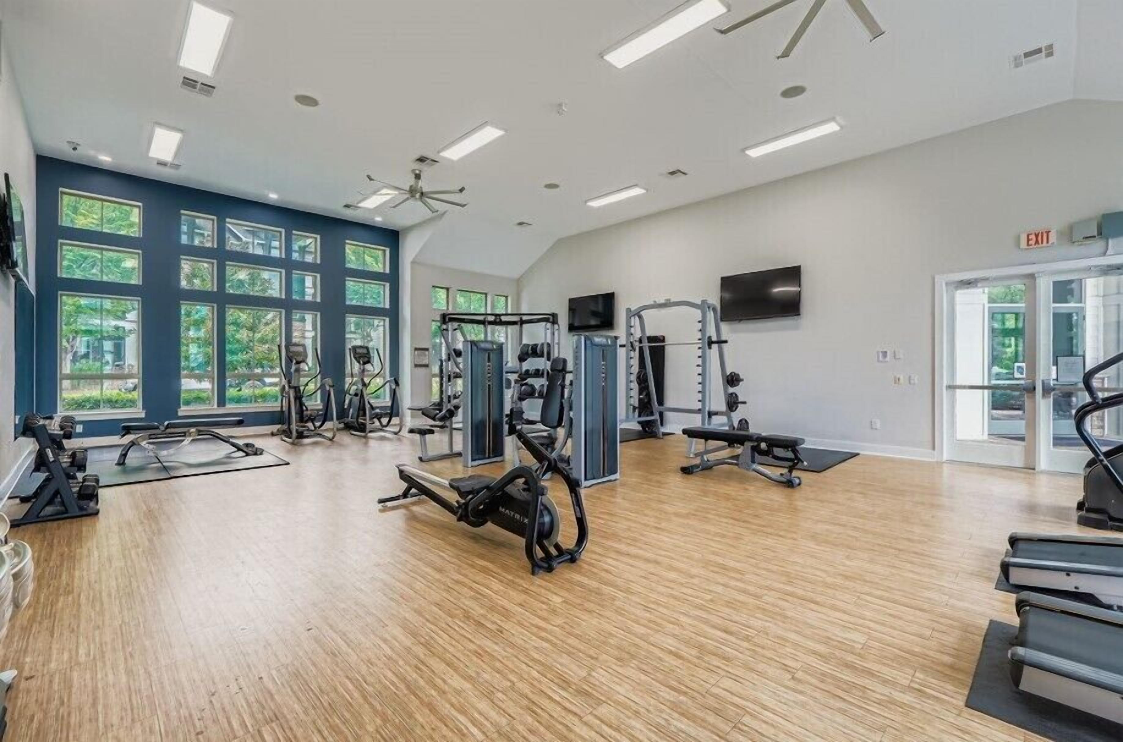 A gym with various exercise equipment, large windows, and a ceiling fan.