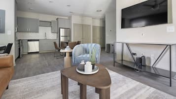 Un salón moderno con un sofá, una mesa de centro con adornos, un televisor montado en la pared y una cocina al fondo.