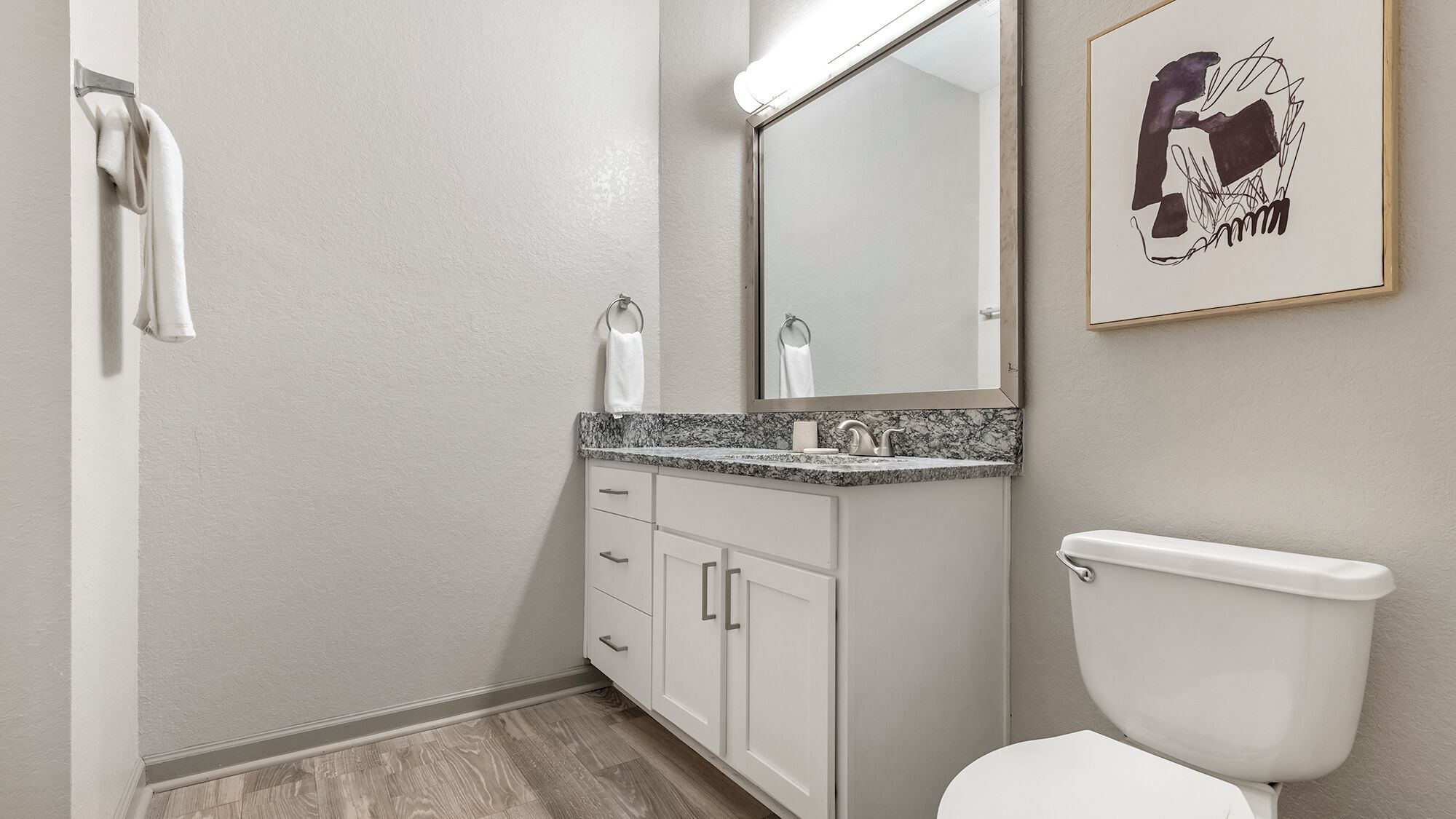 Un baño con inodoro blanco, encimera de mármol, lavabo y espejo.