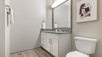 A bathroom with a white toilet, a marble countertop, a sink, and a mirror.