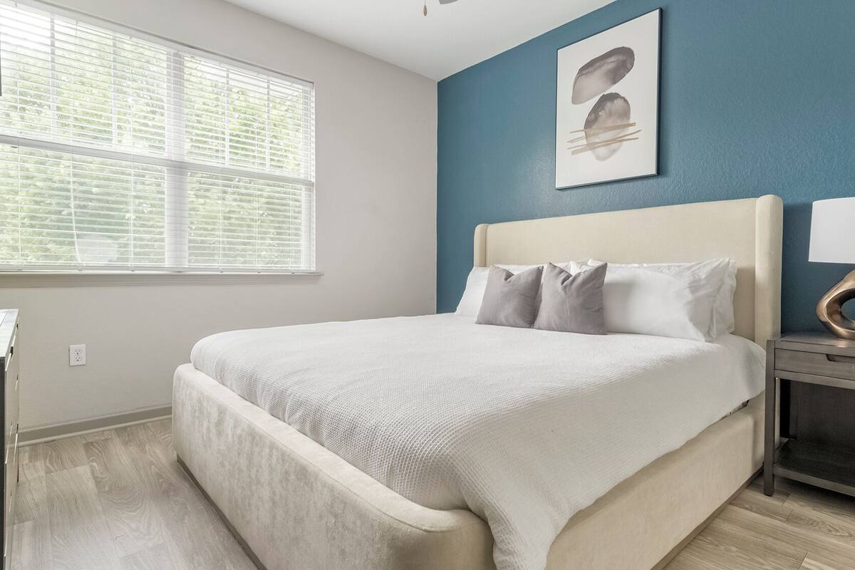 A bedroom with a bed, a nightstand, a lamp, and a window with blinds.