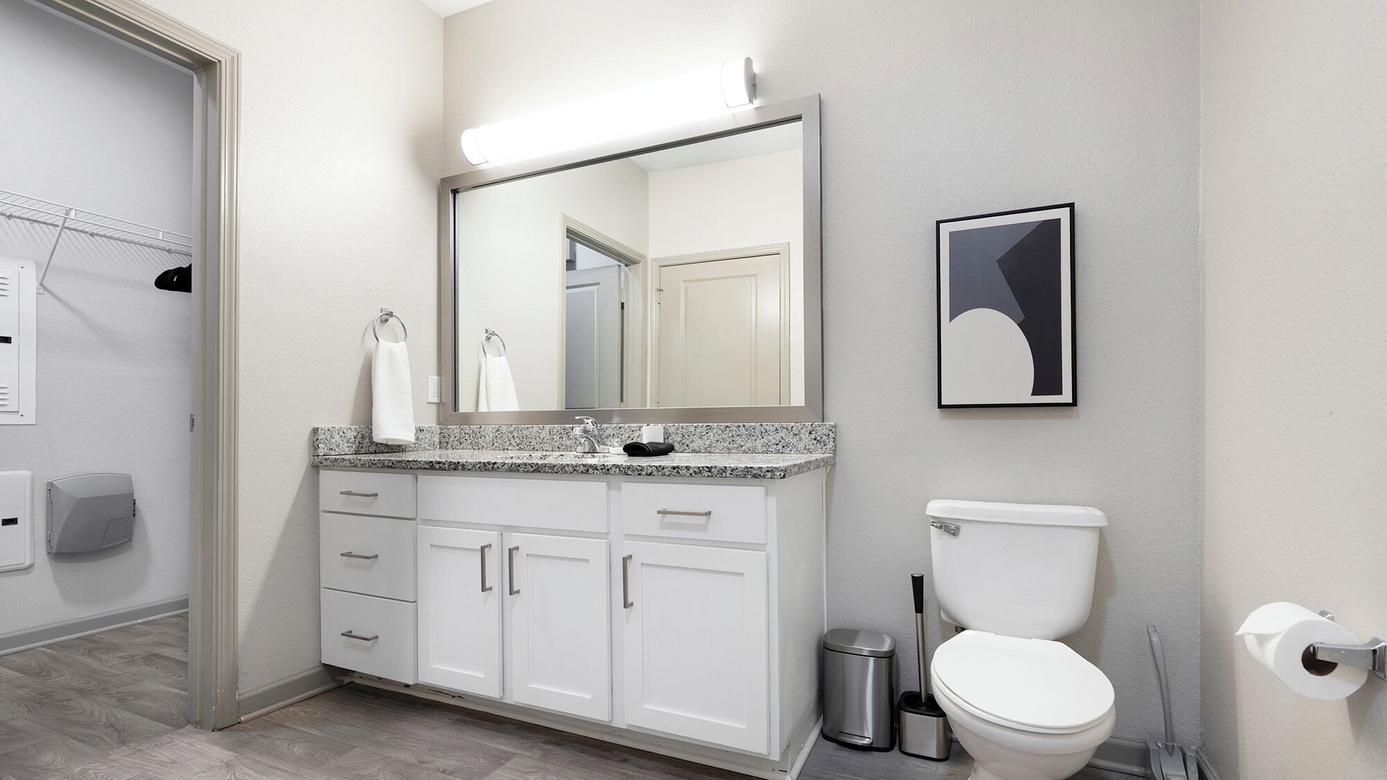 A modern bathroom with a white vanity, a large mirror, a toilet, and a trash can.