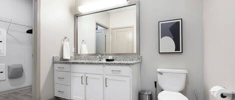 A modern bathroom with a white vanity, a large mirror, a toilet, and a trash can.