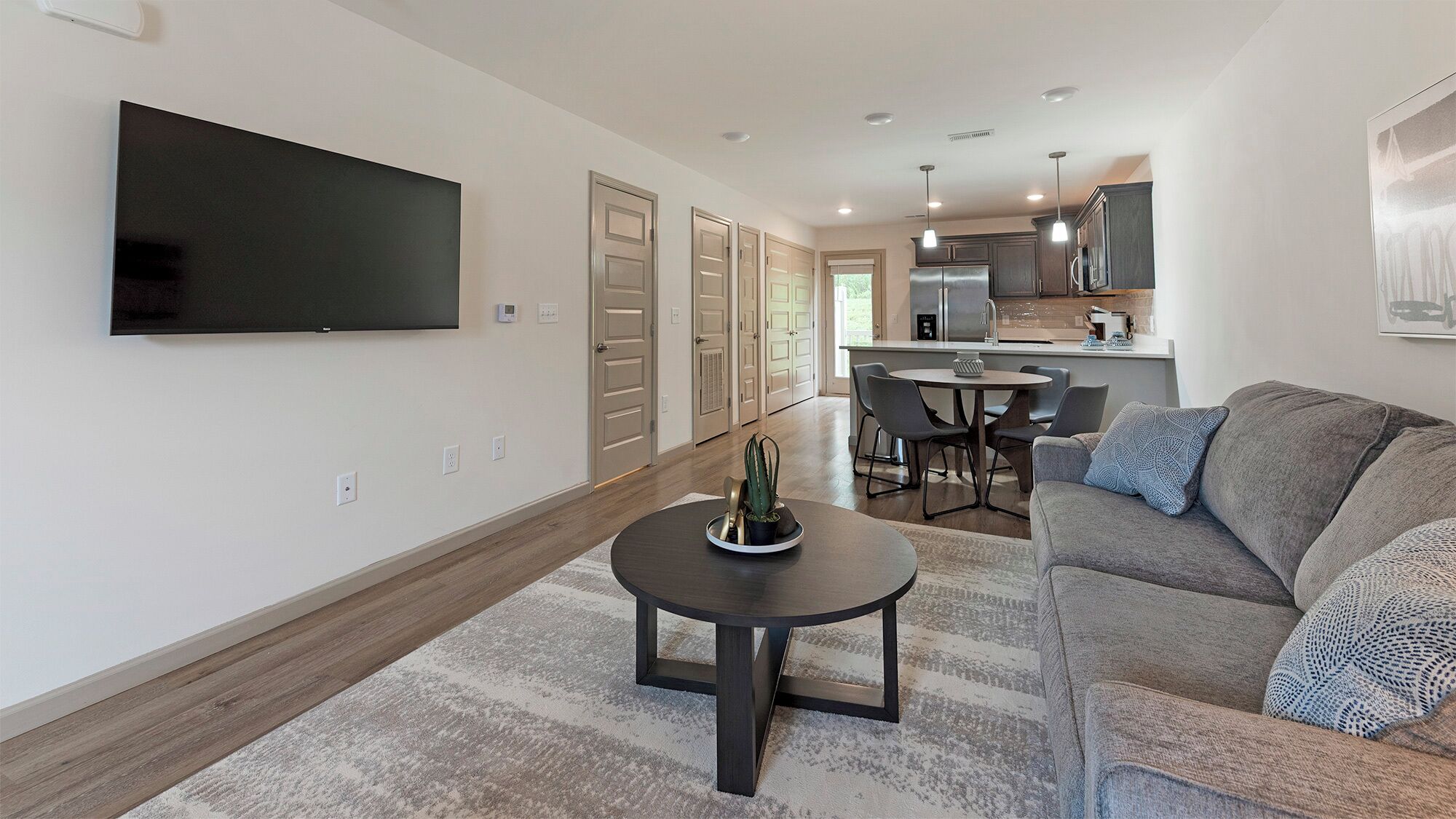 A modern living room with a flat-screen TV, a round coffee table, and a grey sofa.