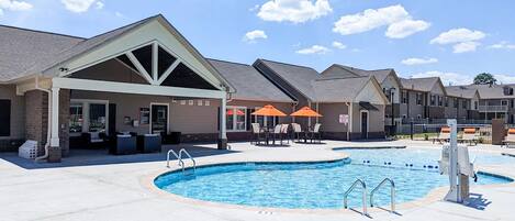 A pool area with a covered seating area, lounge chairs, and umbrellas.