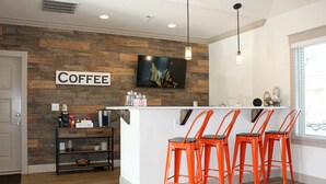 A modern kitchen with a coffee bar, wooden wall, and three orange bar stools.