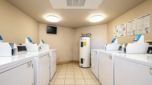 Une buanderie équipée de plusieurs machines à laver, d’un chauffe-eau et de panneaux d’information affichés sur les murs.