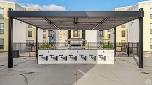 Un espace extérieur aménagé en terrasse, avec un coin salon couvert, un barbecue et une vue sur les bâtiments environnants.