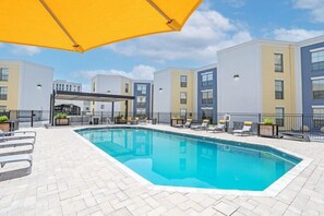 Une piscine entourée de bâtiments à plusieurs étages dotés de balcons, avec des chaises longues et des parasols à proximité.