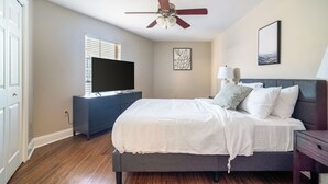 Une chambre à coucher avec un lit, un ventilateur de plafond, un téléviseur posé sur une commode et des œuvres d’art accrochées aux murs.