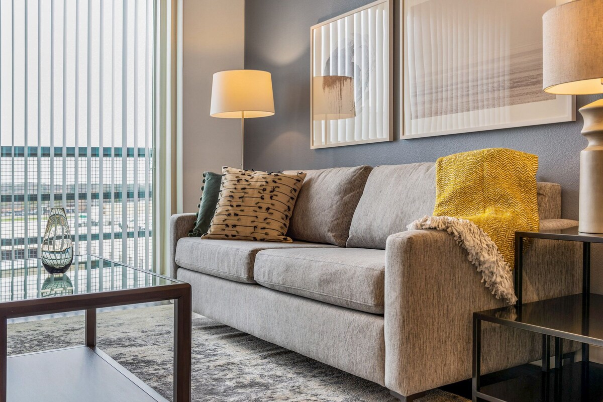 A modern living room with a grey sofa, two lamps, and a glass coffee table.