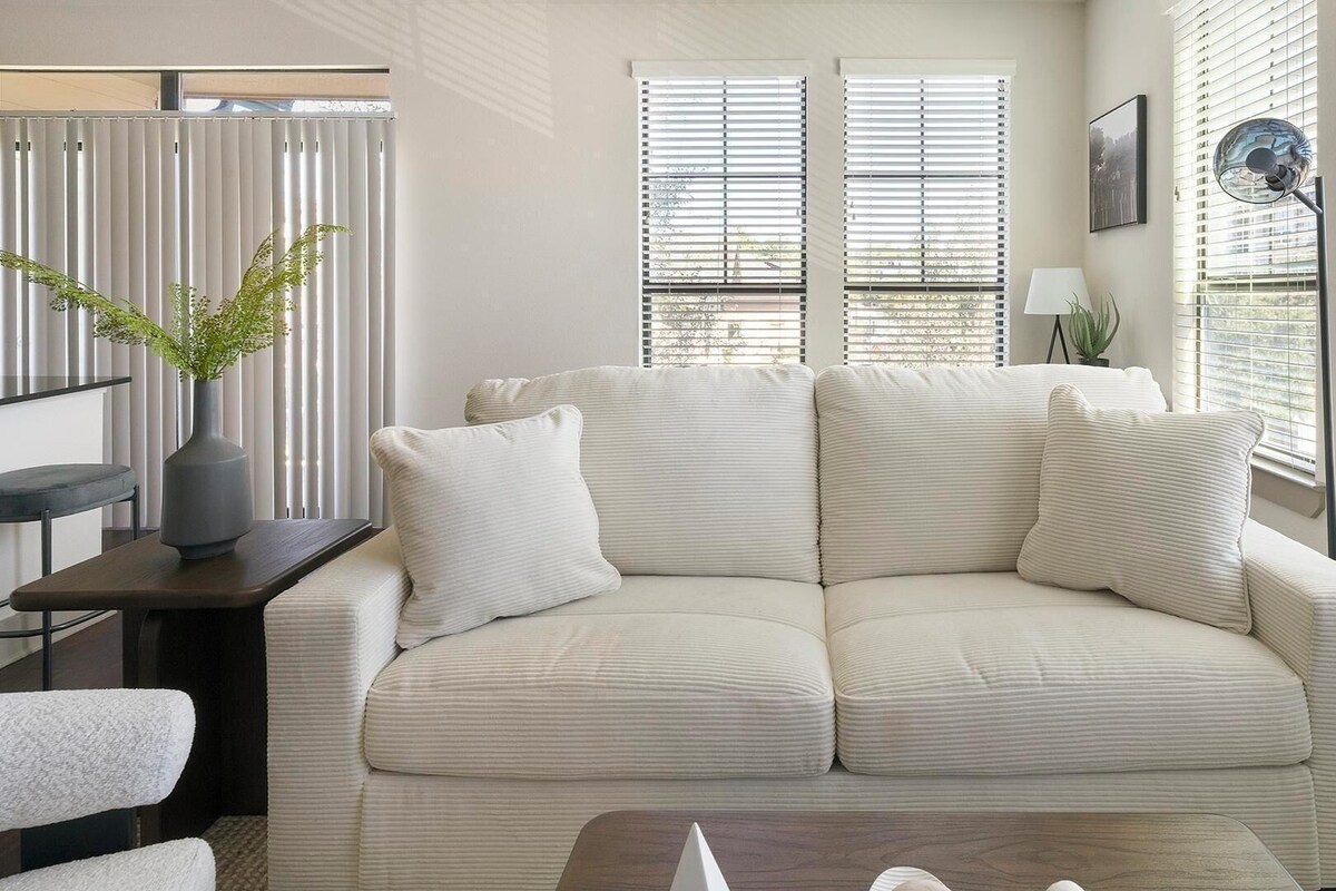 A modern living room with a beige sofa, a small side table, a lamp, and a potted plant.