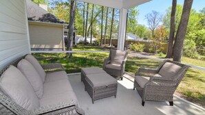 Une terrasse couverte, aménagée avec des meubles en osier, notamment un canapé et des fauteuils, donnant sur un jardin avec des arbres et une pelouse.