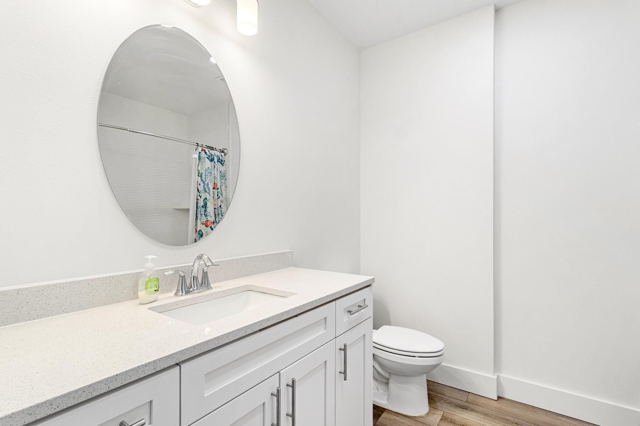 Une salle de bain moderne avec un lavabo blanc, un miroir rond et des toilettes.
