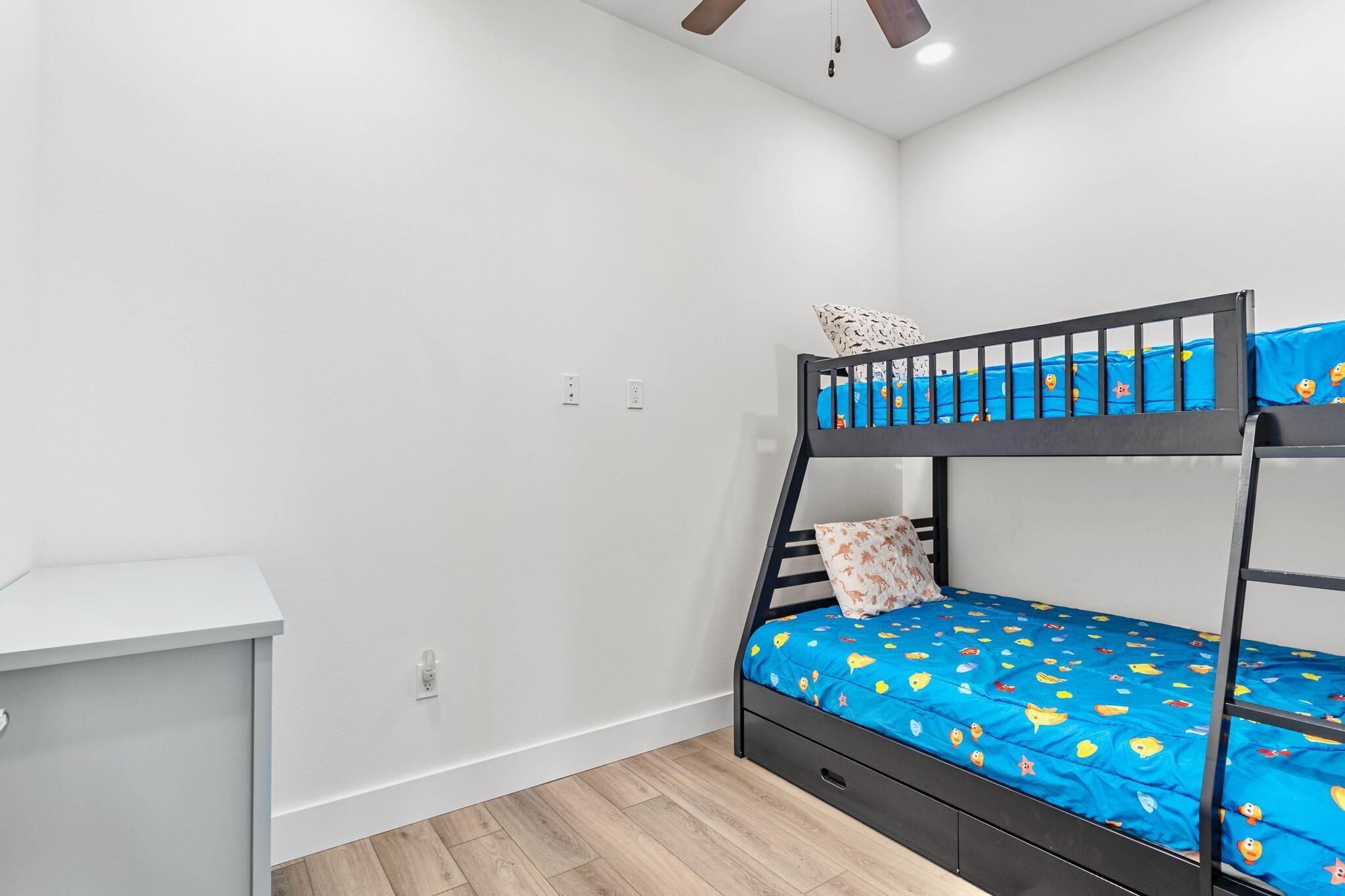 A bunk bed with a blue mattress and a white pillow, a small desk, and a light-colored wall.