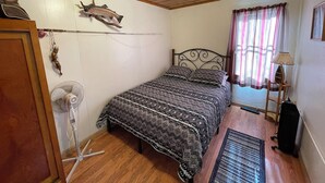 A bedroom with a bed, a fan, a lamp, and a window with curtains. - Stoney River Lodge - Unit 7 - Fisherman (Loveland)