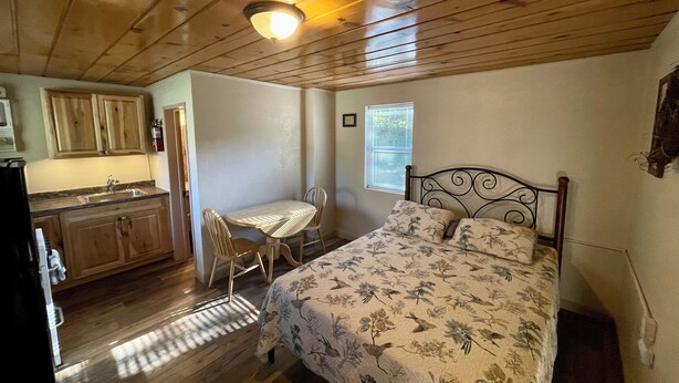 A compact bedroom with a bed, a small table, and a kitchenette.