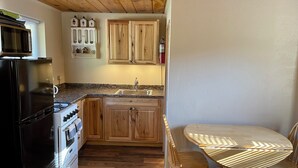A compact kitchen with wooden cabinets, a gas stove, and a sink. There is a dining table with chairs and a microwave above the stove.