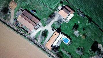 An aerial view of a property with two main buildings, a swimming pool, and surrounding green fields.
