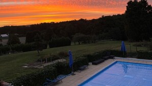 Une piscine avec vue sur le coucher du soleil et un espace verdoyant avec des arbres.