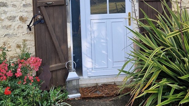 Un bâtiment rustique en pierre, doté d’une porte blanche, de volets en bois et d’une lanterne en métal.