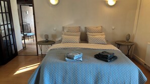 Un lit bien fait, recouvert d’une couette bleue, deux tables de chevet avec des lampes, et une vue sur un balcon.