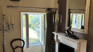Une pièce avec une cheminée, un miroir, une chaise et une fenêtre avec des rideaux.