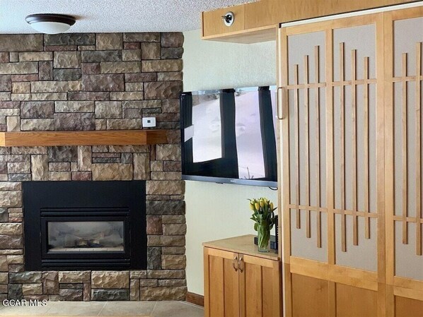 A living room with a stone wall, a fireplace, a television, and a wooden cabinet. - Ski In, Ski Out in Winter Park (Winter Park)