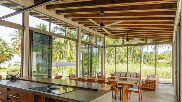 Een moderne keuken met een groot eiland, houten plafond en grote ramen met uitzicht op palmbomen.
