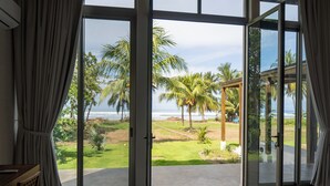 Een kamer met een grote schuifglazen deur die leidt naar een balkon met uitzicht op de oceaan en palmbomen.