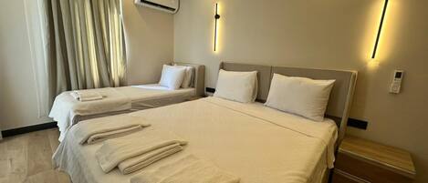 A hotel room with two beds, a ceiling air conditioner, wall-mounted lights, and a bedside table with a lamp.