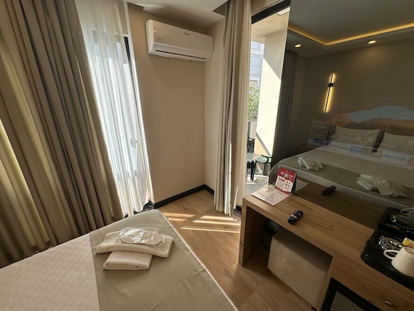 Habitación de hotel con cama, escritorio con teléfono y control remoto, ventana con cortinas, unidad de aire acondicionado y vistas al exterior.