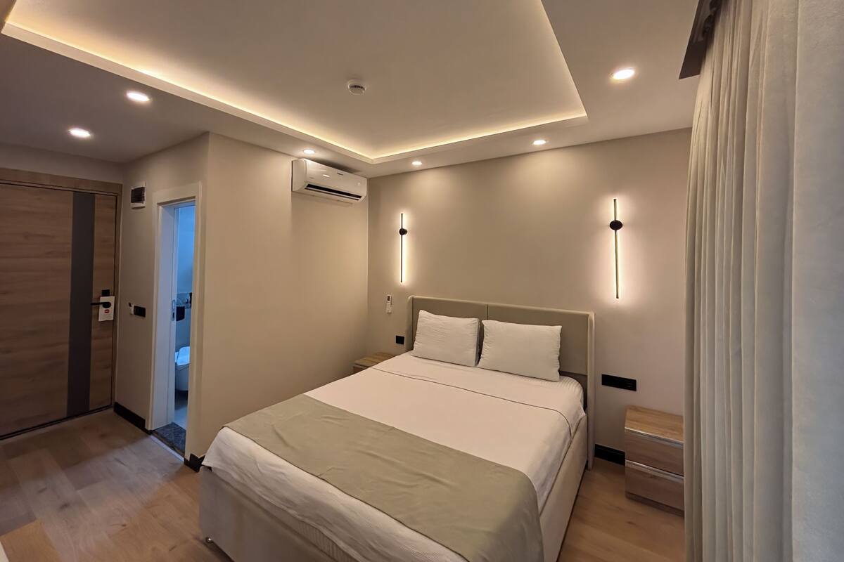 Un dormitori modern amb un llit gran, il·luminació encastada al sostre, un aparell d'aire condicionat i una porta que dona a una altra habitació.