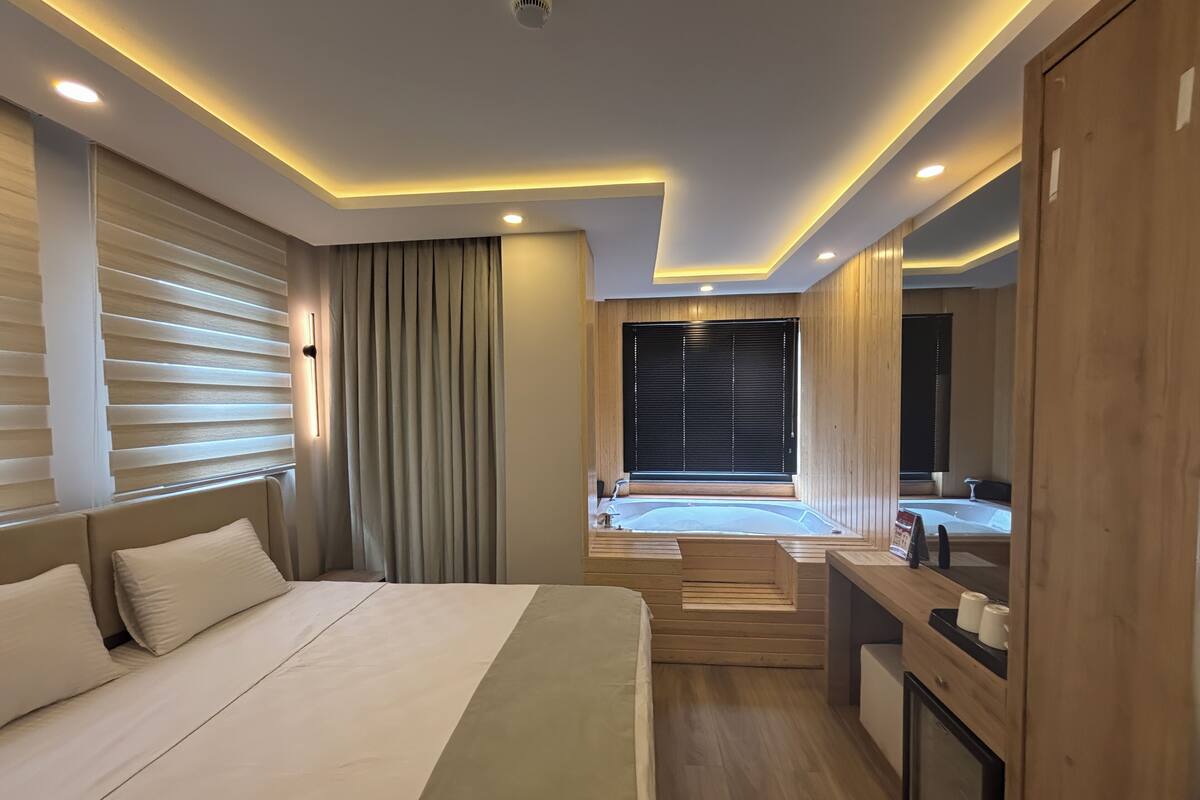 Habitació d'hotel moderna amb un llit gran, una petita zona de seients, una banyera i un armari de fusta.
