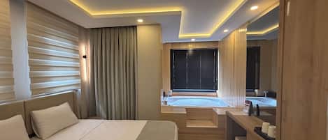Une chambre d’hôtel moderne avec un grand lit, un petit coin salon, une baignoire et une armoire en bois.