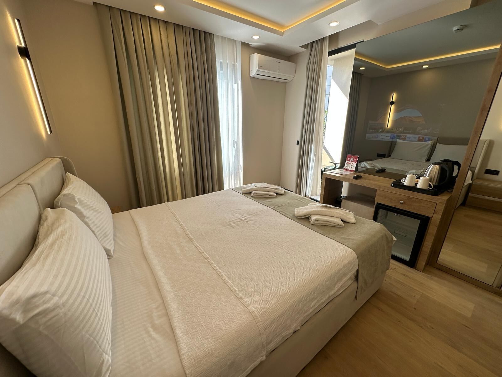 A hotel room with a large bed, a desk with a coffee maker, and an air conditioning unit on the wall.