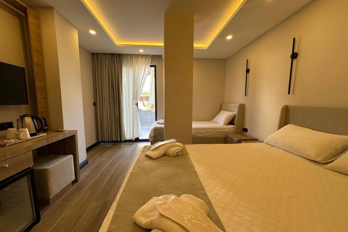 Una habitació d'hotel amb un llit gran, una taula de nit amb cafetera, un televisor i una finestra amb cortines.