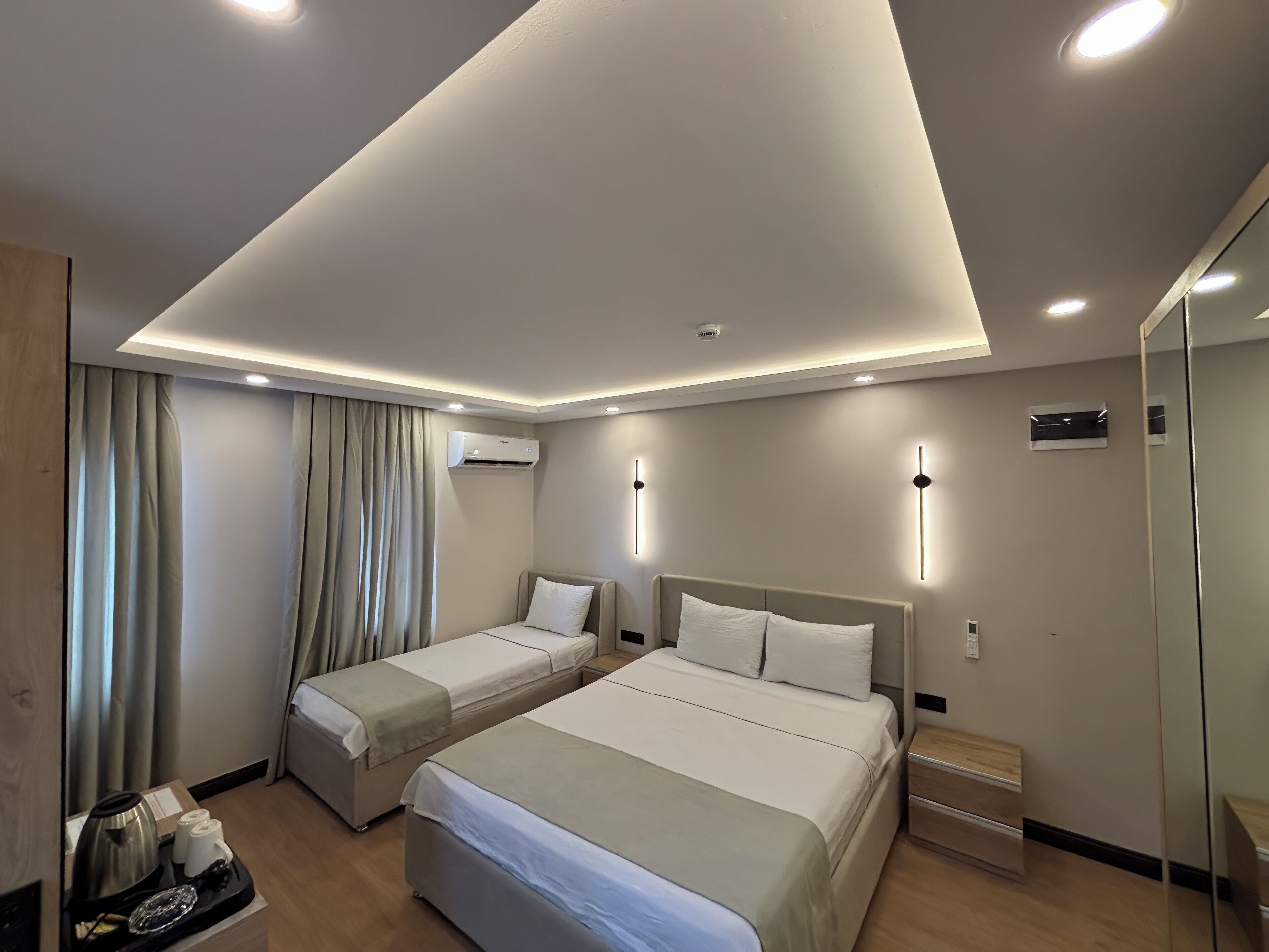 A modern hotel room with two beds, a minibar, and a large mirror.