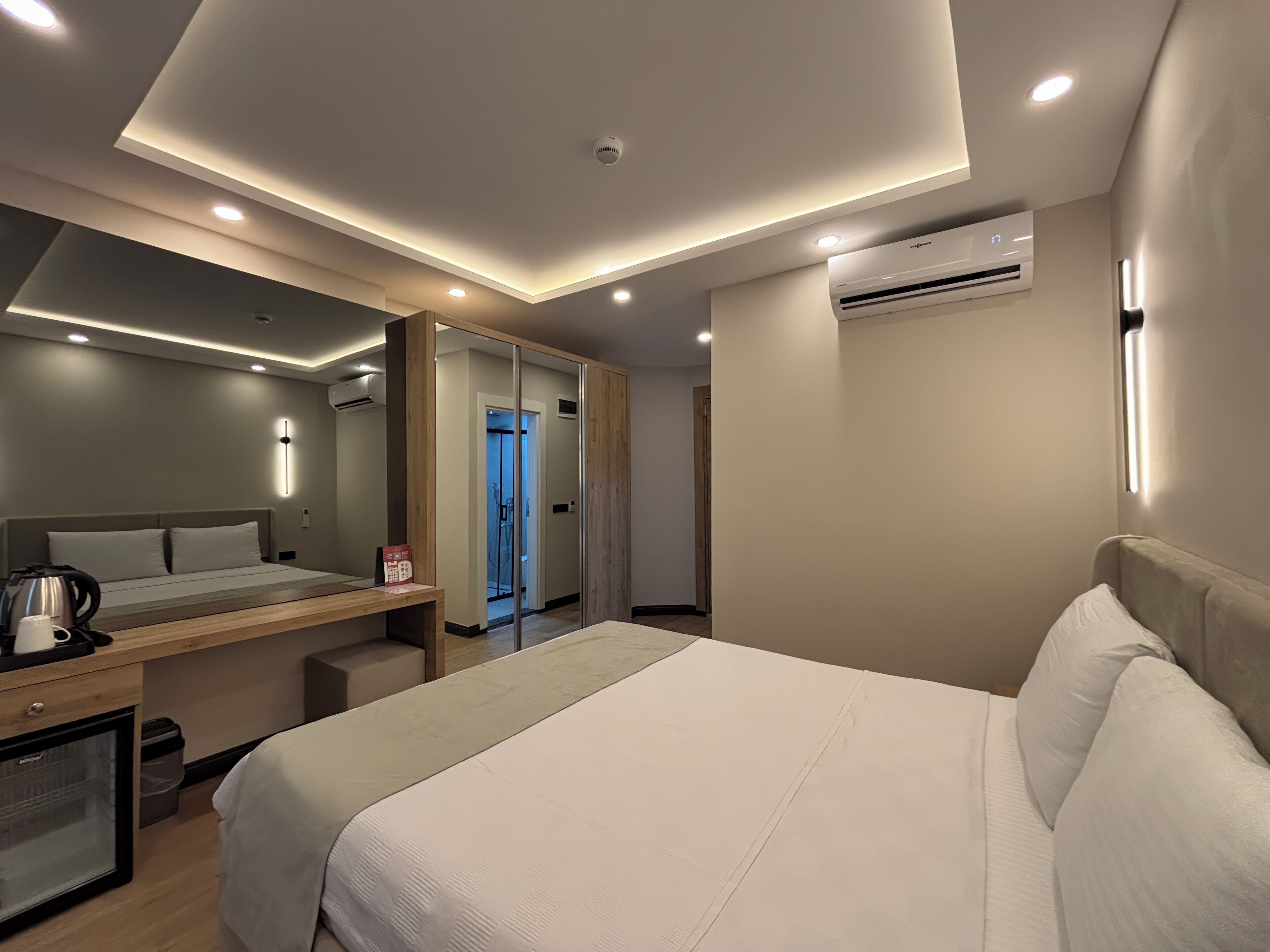A modern hotel room with a large bed, bedside table, and a mirror.
