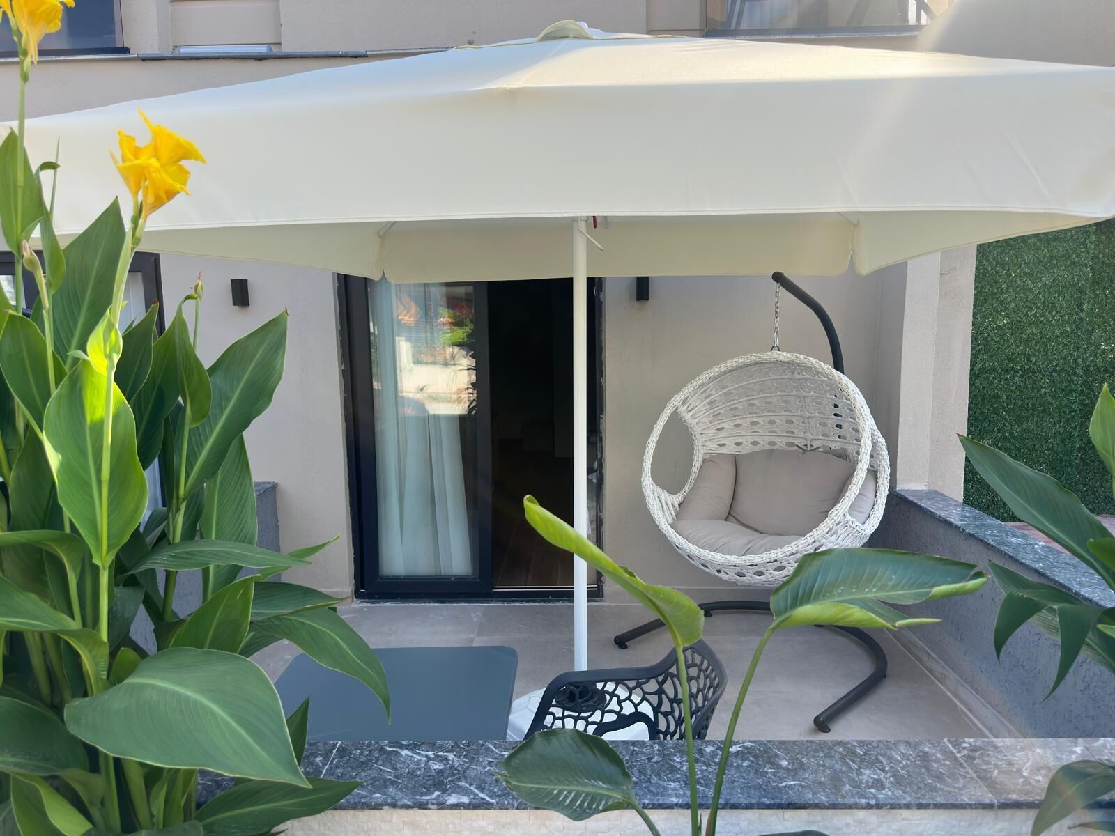 A patio with a hanging chair, a table, and a large umbrella.